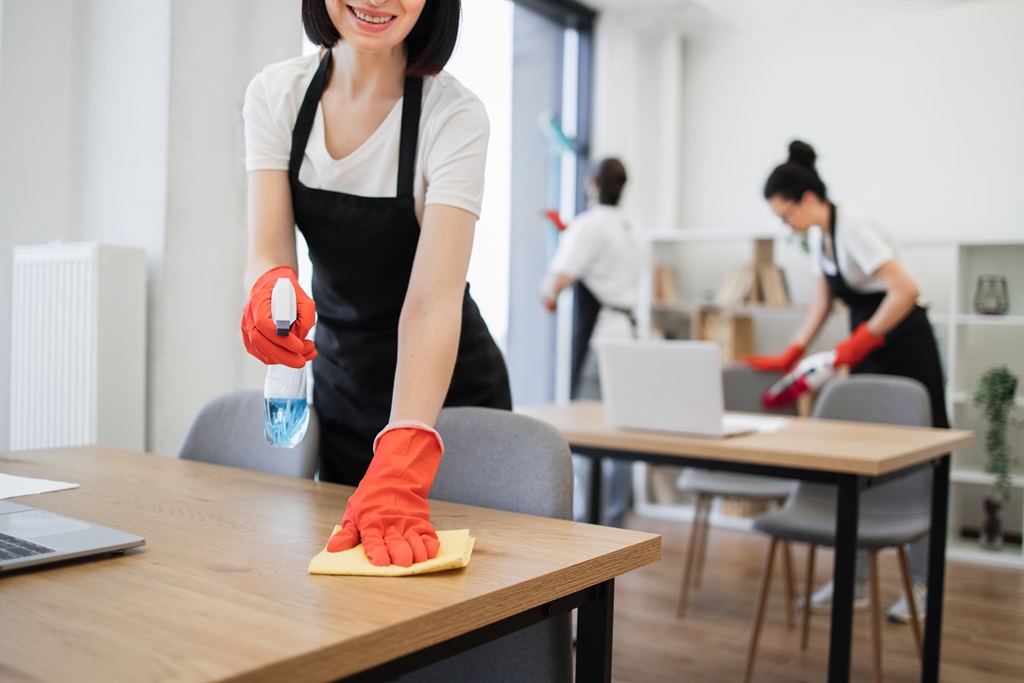 Cropped view of hand with rag and spray of young woman cleaning table in office